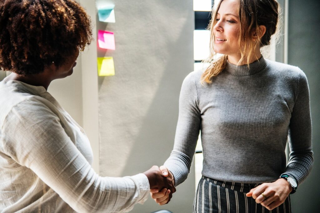 One woman shaking hands with another in meeting room