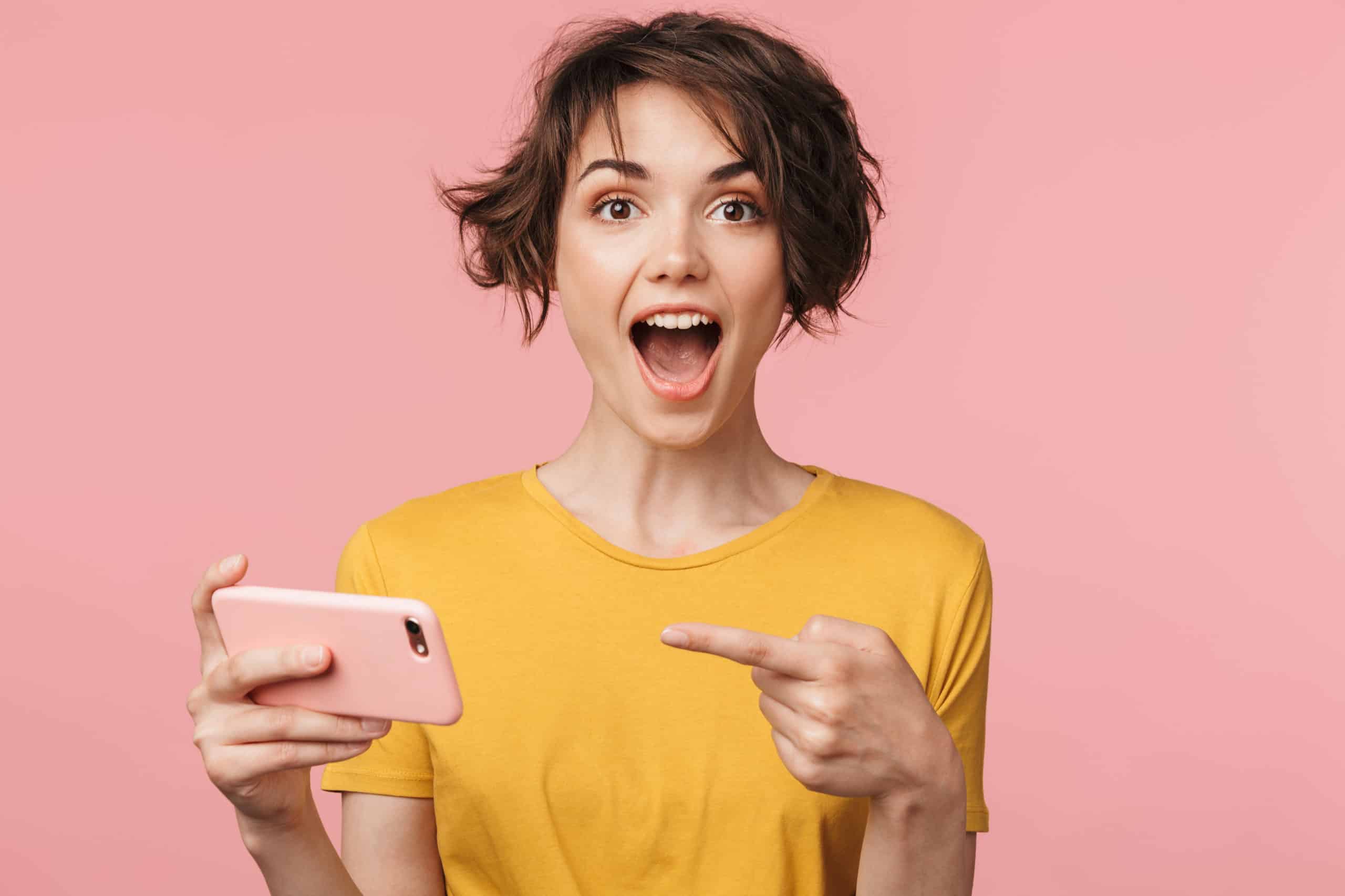 Image of a shocked young beautiful woman posing isolated over pink wall background play games by mobile phone.